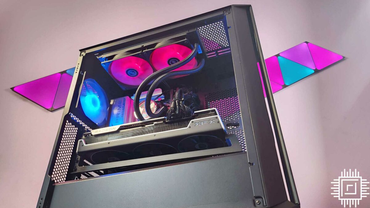 The PCSpecialist Odin TX gaming PC lit up with pink and blue lighting, in front of Nanoleaf Ultra Black Shapes with the same colours.