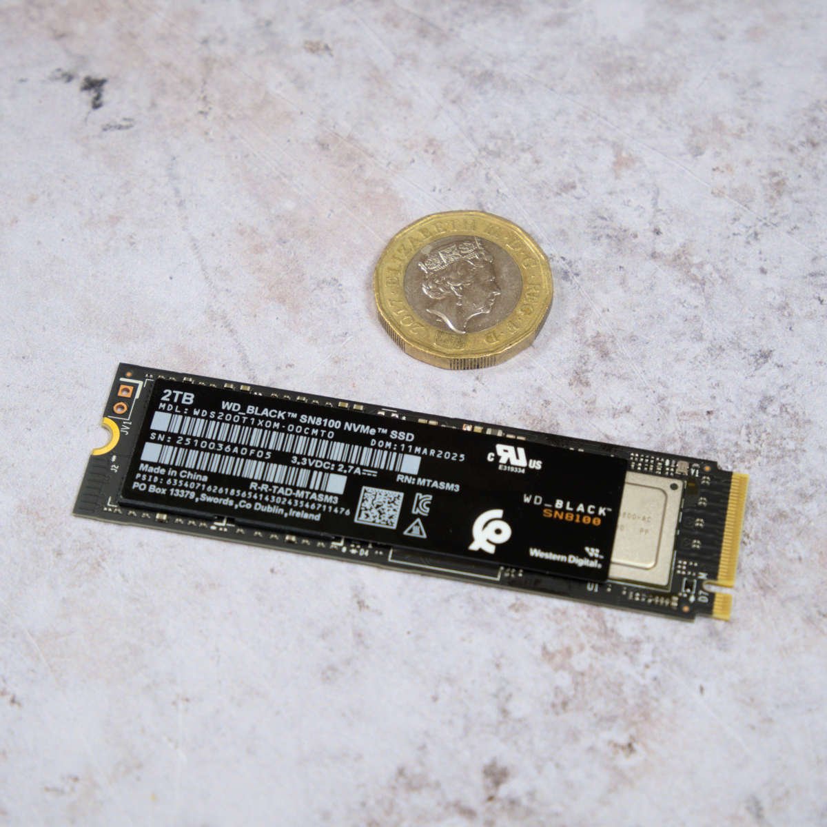 WD_Black SN8100 2TB SSD lying next to a £1 coin.
