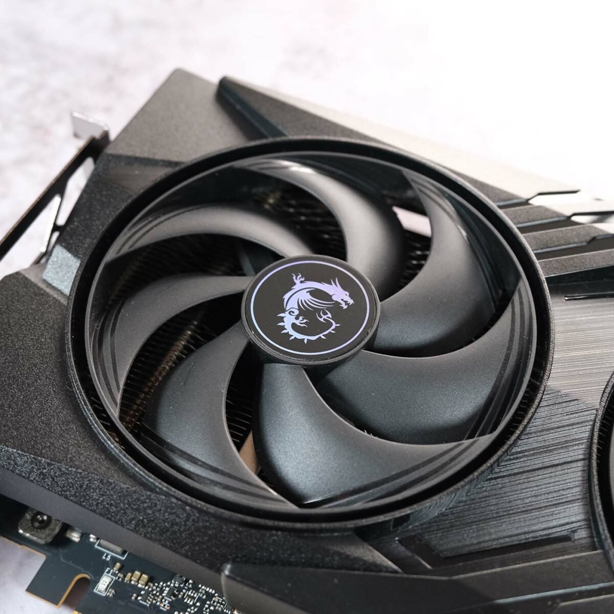 Close up of MSI GeForce RTX 5060 Gaming OC fan, its holographic dragon logo reflecting light.