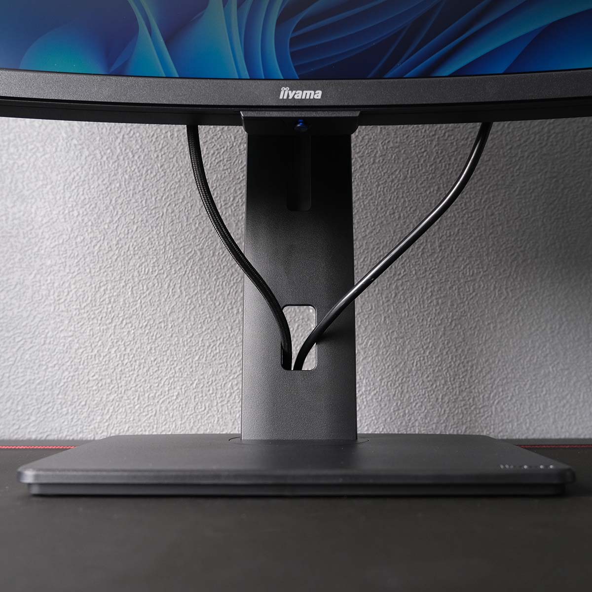 A close up of iiyama ProLite XCB3497WQSNPH-B1's arm and base, with two cables flowing through the grommet.