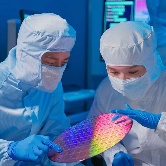 Two people in clean suits, hold a chip wafer between them.