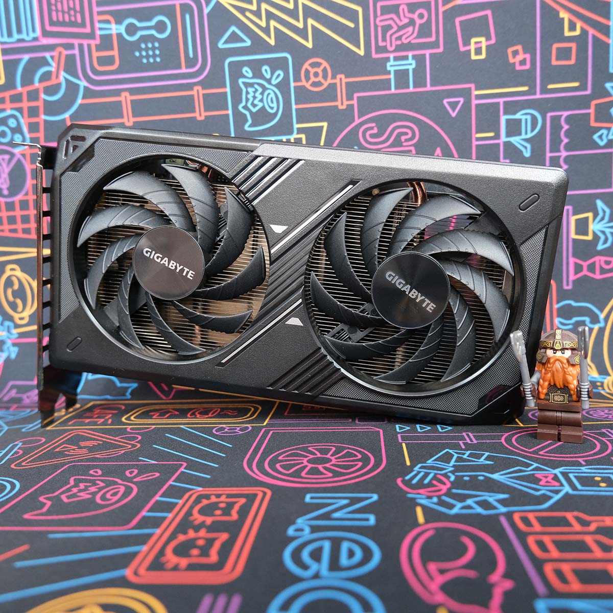 Gigabyte GeForce RTX 5050 Windforce OC graphics card stands upright, horizontally, its frontplate facing the camera with a small Lego figurine to its right.