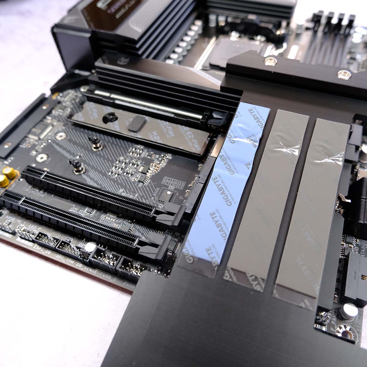 The lower portion of Gigabyte X870E Aorus Elite X3D, the motherboard's large heatsink is removed showcasing included heat pads and slots.