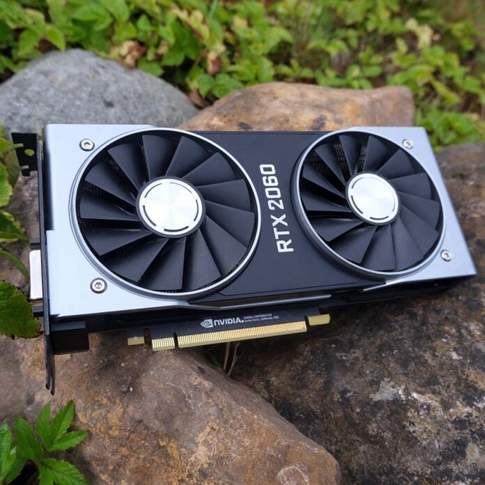 Nvidia GeForce RTX 2060 Founders Edition graphics card lying atop some rocks, surrounded by greenery.