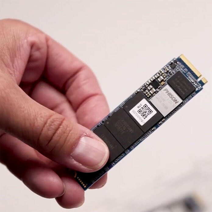 A hand holding an NVMe M.2 SSD, using a Phison NAND flash memory controller.