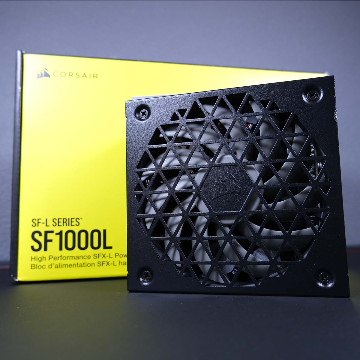 A Corsair SF100L power supply, standing upright in front of its retail packaging.