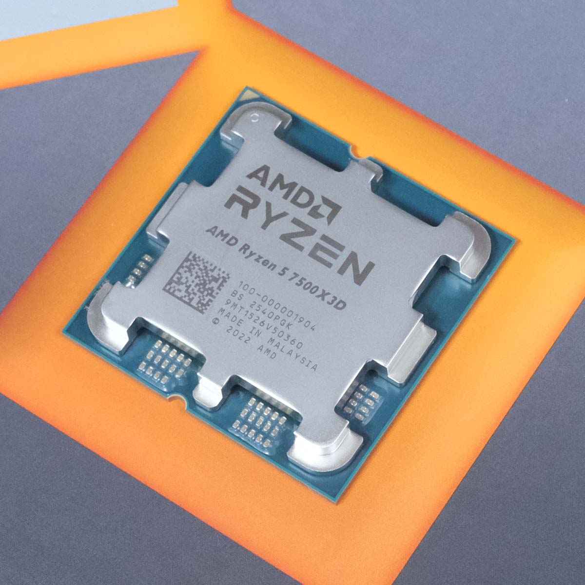 An AMD Ryzen 5 7500X3D laying on top of its retail packaging, surrounded by an orange square.