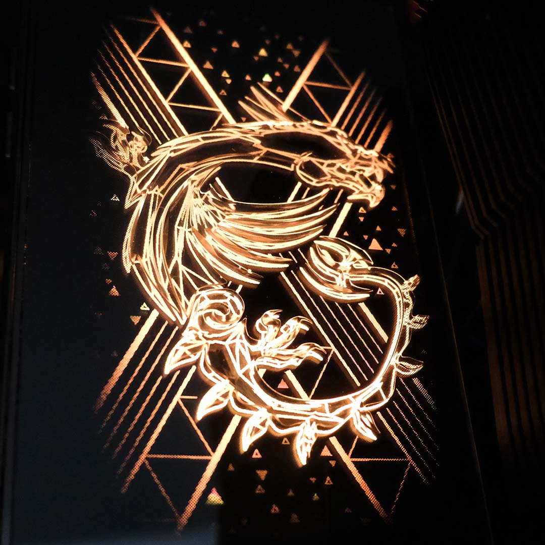 A top-down shot of the stereoscopic dragon on the MSI MEG X870E Godlike X motherboard, lit up gold.