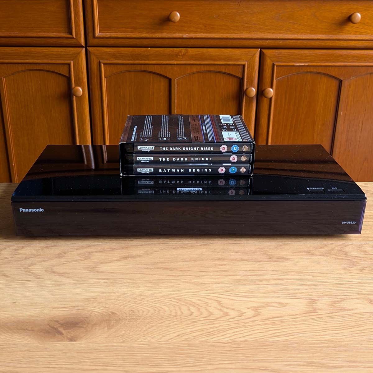 A Panasonic DP-UB820 4K Blu-ray player, sat atop a wooden surface, with a trio of Blu-ray discs sat atop it.