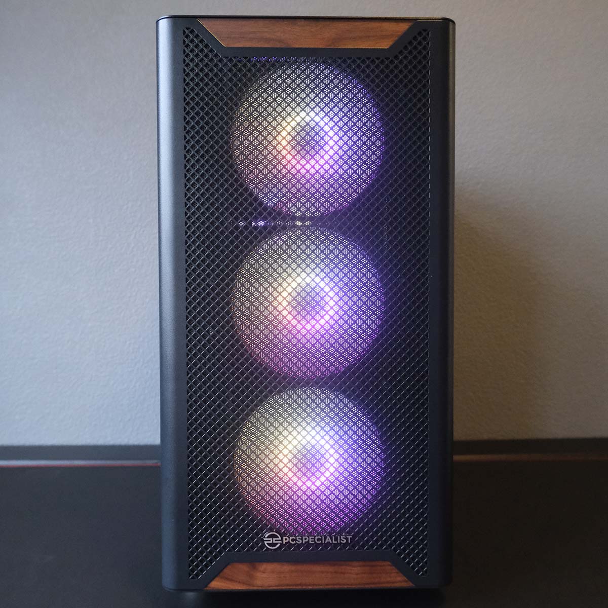 A front-on view of the PCS Aegis Black ARGB chassis, its three intake fans glowing pink and yellow.
