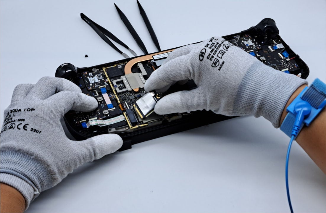 Two gloved hands working on a Steam Deck, its internals exposed.