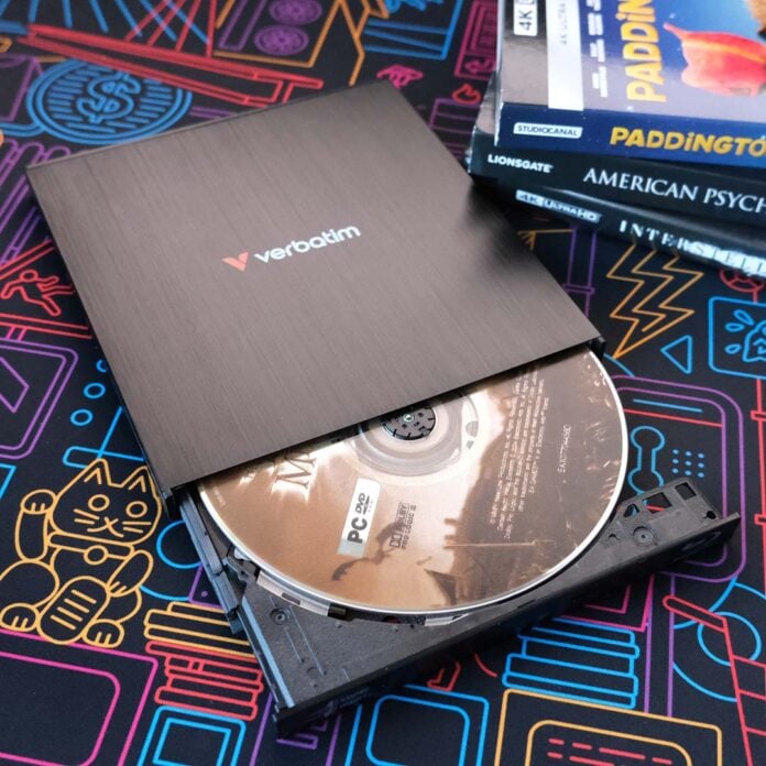 A disc drive, tray partially open, with a DVD inside it with 4K Blu-Rays to its right.