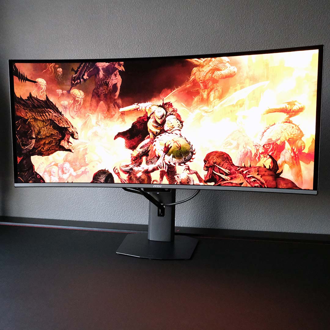 The MSI MPG 341CQR QD-OLED X36 standing atop a desk, displaying a Doom the Dark Ages wallpaper.