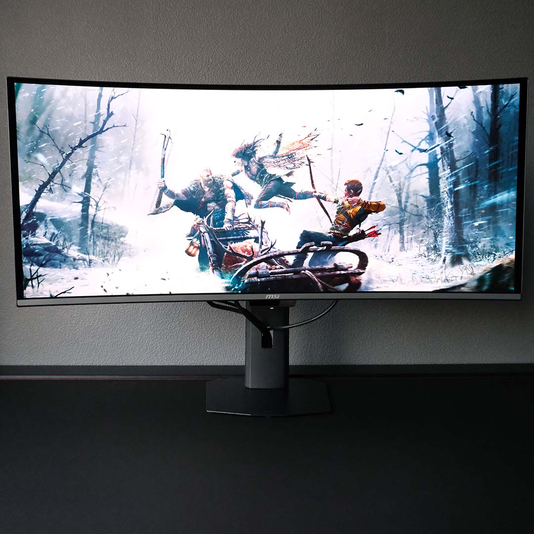 The MSI MPG 341CQR QD-OLED X36 standing atop a desk, displaying a God of War wallpaper.
