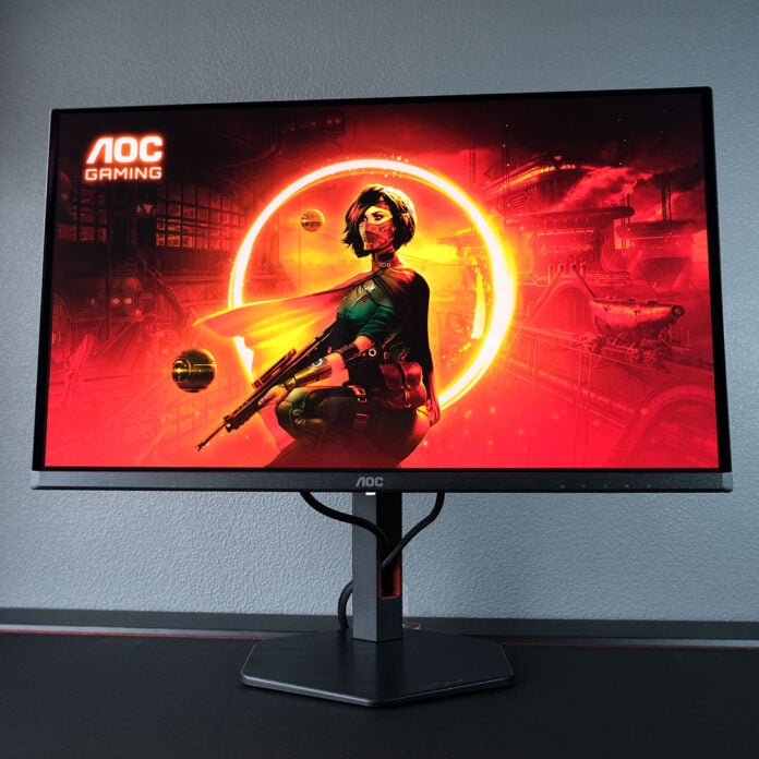 An AOC Q27G4SDR monitor displays a red-orange background, featuring a female-presenting sci-fi character.