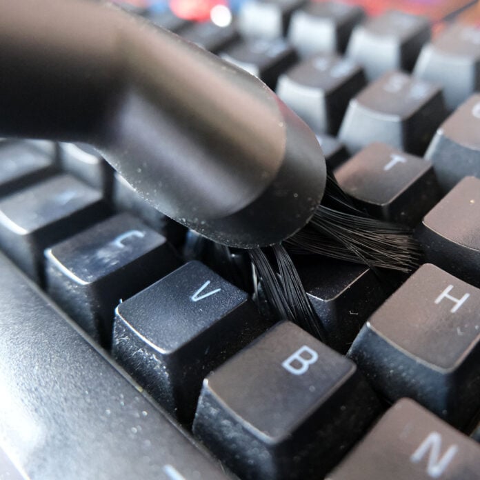 A brush head reaches in between the cracks of keyboard keycaps.