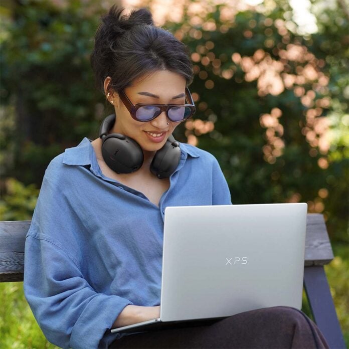 A person using a Dell XPS 13 on their lap, on an outdoor bench.