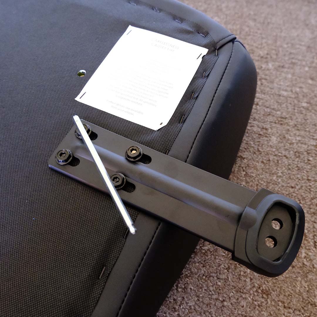 A hex key, tightening the screws that attach the arm base of the Thunder X3 Solo gaming chair to its seat cushion.