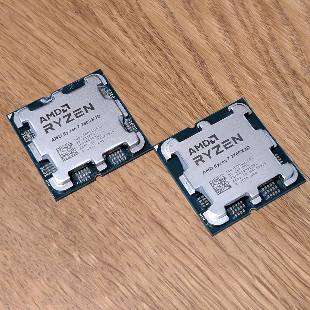 An AMD Ryzen 7 7800X3D (top left) and Ryzen 7 7700X3D (bottom right), atop a wooden backdrop.